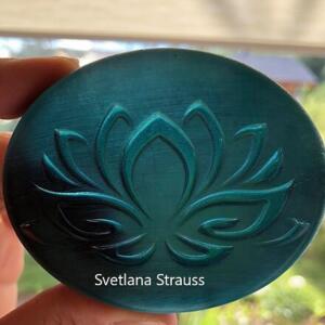 A teal blue round disc with a raised, engraved design of a lotus flower. The disc has a brushed metal finish and the text "Svetlana Strauss" is printed at the bottom.