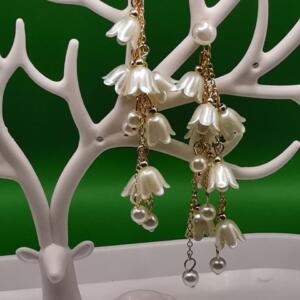 A pair of long, dangling earrings with white flower-shaped charms and gold chains. The earrings are displayed on a white deer-shaped stand.