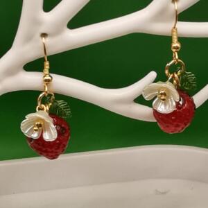 A pair of gold dangle earrings with red and white strawberry charms and green leaves.