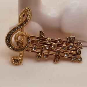 A gold-tone brooch featuring a treble clef and musical notes, adorned with clear rhinestones.