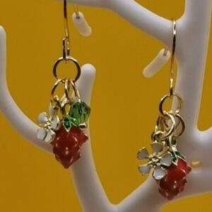 Gold dangle earrings with a red and green strawberry charm and a white flower.