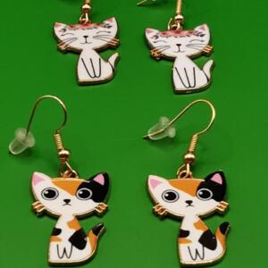 A pair of gold cat earrings. One pair features a white cat with a pink flower crown and the other pair features a calico cat.