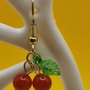 Gold dangle earrings with a red cherry design. The earrings feature two red cherries with a green leaf.