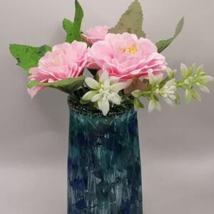 A bouquet of pink flowers with white flowers and green leaves in a blue and green patterned glass vase.