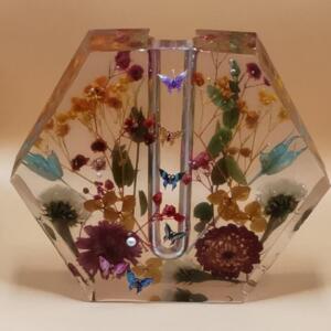 A hexagonal clear resin vase with a clear glass tube in the centre. The vase is filled with dried flowers and butterflies in shades of pink, purple, blue, yellow, and green.