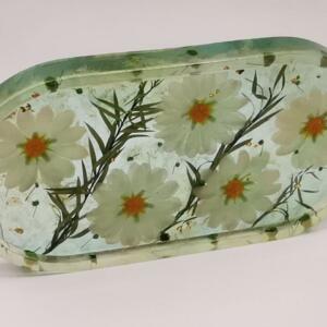 Oval-shaped clear resin tray with a green border and white flowers pressed inside. The flowers have orange centres.