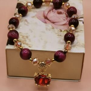 A red and gold bracelet with a red gemstone charm. The bracelet is made of tiger's eye beads and crystal beads.