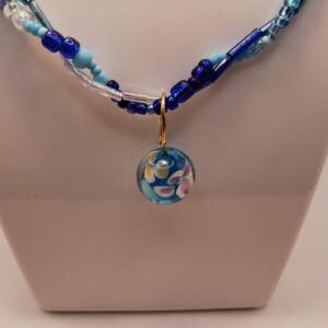 A multi-strand necklace with blue and white beads and a small, round pendant with a blue and white floral design.
