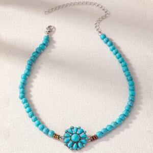 A turquoise blue beaded necklace with a silver flower charm. The necklace is made of small, round beads and has a simple, elegant design.