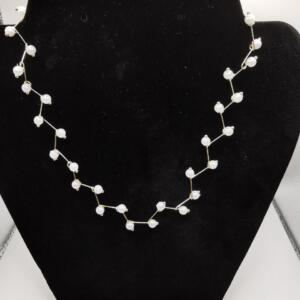 A delicate gold necklace with white pearl accents. The necklace is arranged in a zig-zag pattern.
