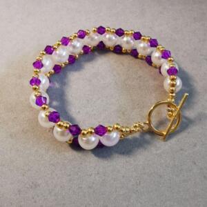 A gold bracelet featuring white pearls and purple beads. The bracelet has a toggle clasp.