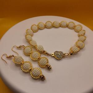 A gold necklace and earrings set with white pearl beads. The necklace has a heart-shaped pendant with clear rhinestones.