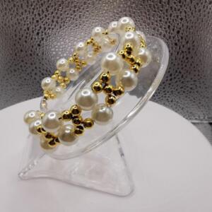 A white pearl and gold bead bracelet. The bracelet is on a clear display stand.
