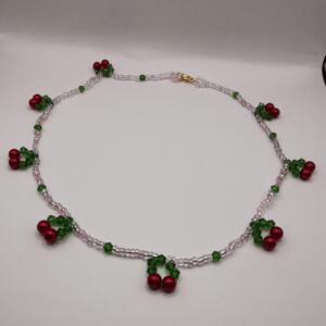 A delicate necklace made of small white and pink beads with green and red beads forming cherry designs.